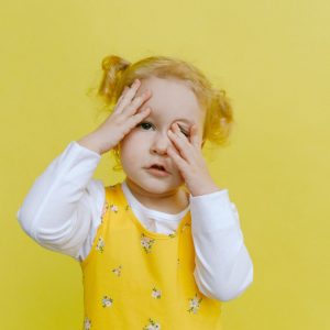 little girl wearing yellow dress with hands covering eyes